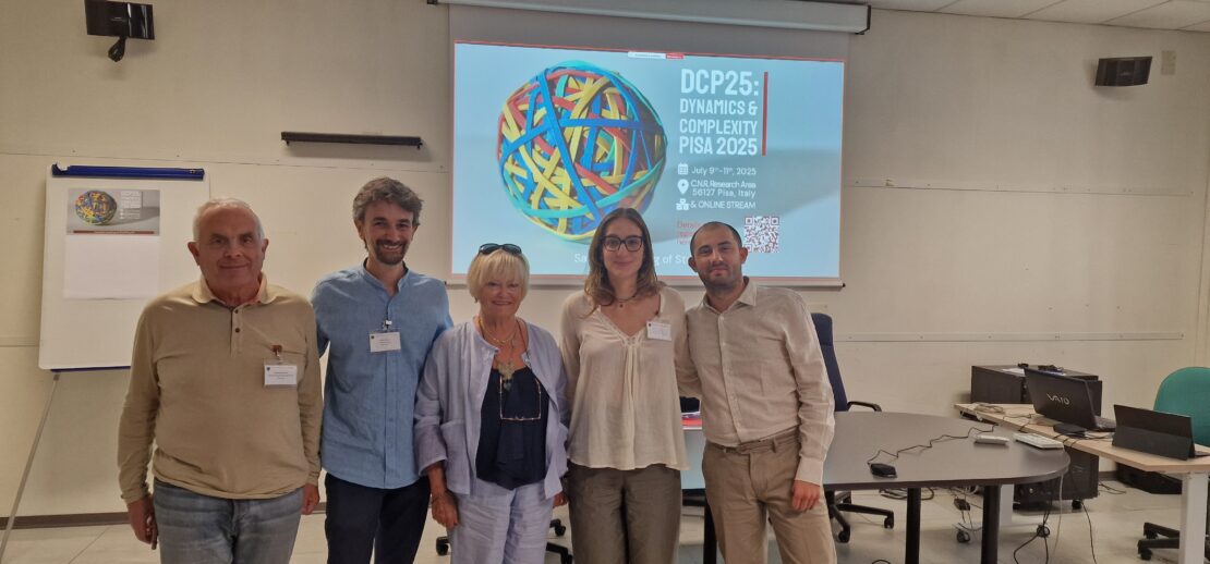 I vincitori del premio nell'aula della premiazione, davanti a una scrivania, con sullo sfondo la locandina del workshop DCP25.